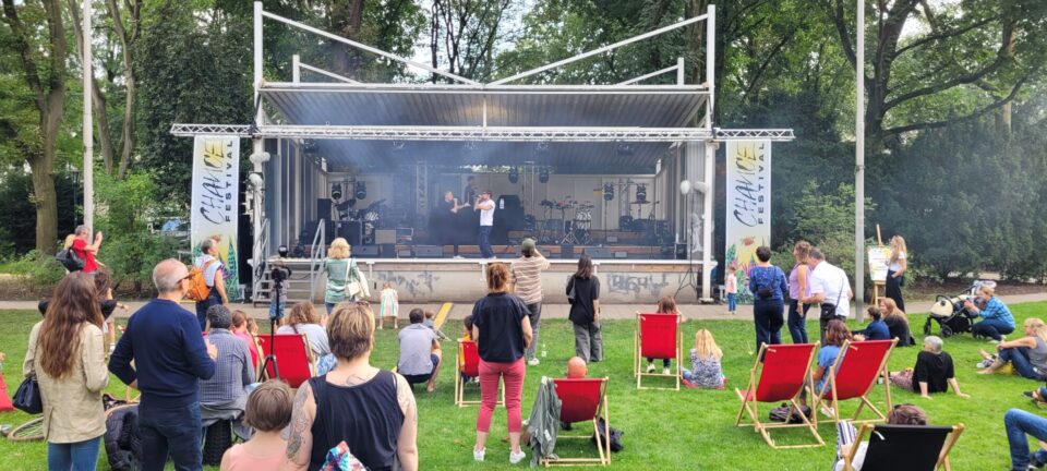 Das Musikpavillon des Hofgartens in Düsseldorf, wo eine band auftritt und Menschen davor stehen oder sitzen.