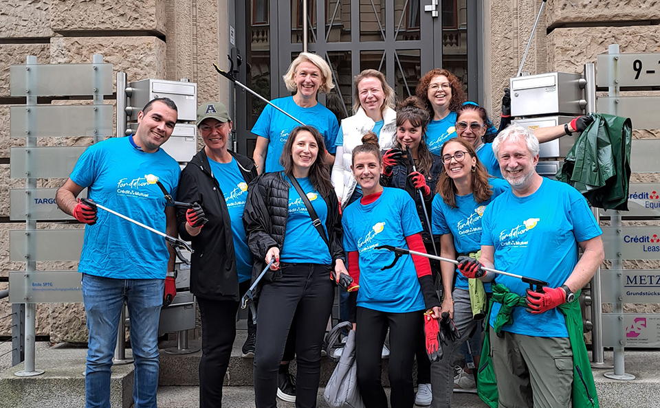 Das Team der CIB der TARGOBANK steht vor ihrem Bürogebäude und hält Utensilien zum Müll aufsammeln in der Hand.