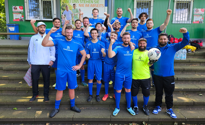 Ein Gruppenbild von der TARGOBANK Fußballmannschaft und die Spieler heben jeweils einen Arm in die Luft.