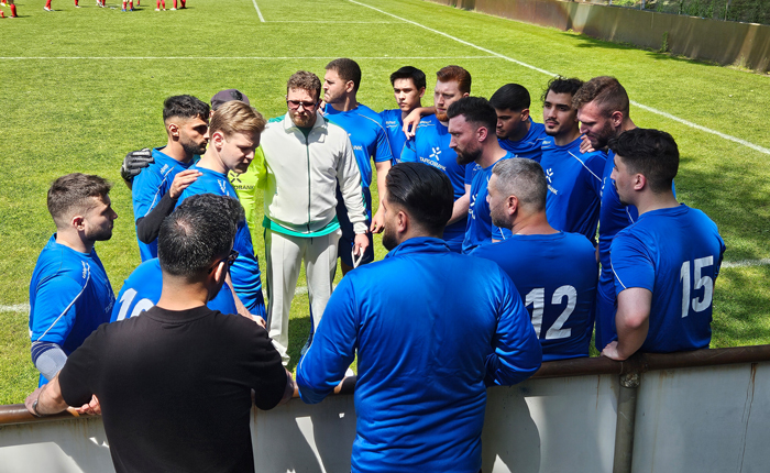 Die Spieler der TARGOBANK Fußballmannschaft stehen auf dem Fußballfeld in einem Kreis und der Trainer steht in der Mitte.