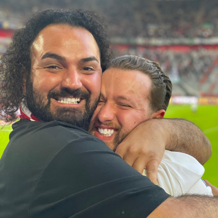 Zwei Spieler der TARGOBANK Fußballmannschaft umarmen sich in dem Fortuna Fußballstadion und lächeln dabei in die Kamera.