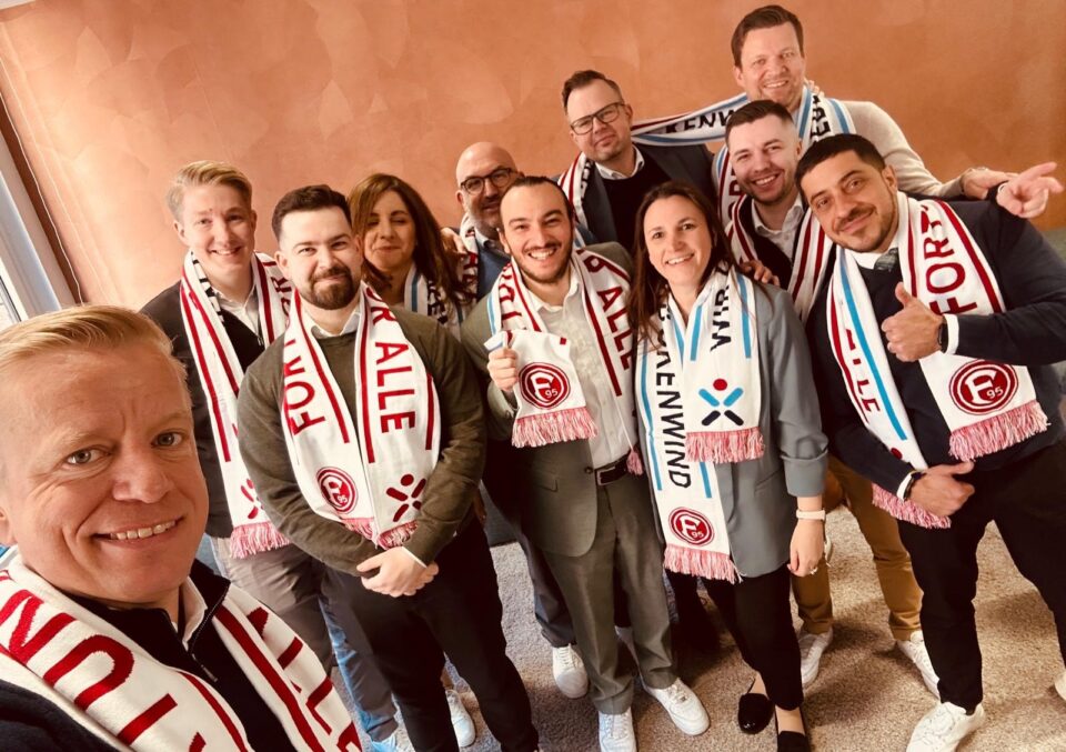 Eine Gruppe von Personen steht zusammen und lächelt für ein Foto. Alle tragen Schals mit dem Aufdruck 