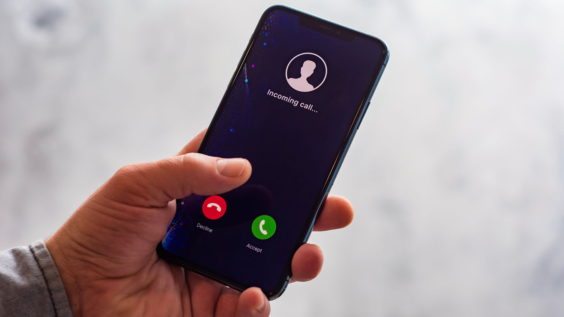 Ein Smartphone mit einem eingehenden Anruf wird in einer Hand gehalten. Der Bildschirm zeigt einen Anruf mit der Aufschrift 