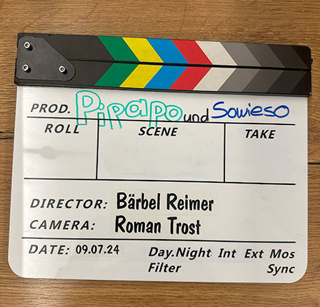 Ein Klappbrett mit der Aufschrift 'Pipapo und Sowieso'. Die Felder enthalten Informationen zu Roll, Szene und Aufnahme. Der Regisseur ist Bärbel Reimer und die Kamera wird von Roman Trost geführt. Das Datum ist der 09.07.24. Es sind auch technische Hinweise wie Tag/Nacht und Int. Ext. Mos Sync aufgelistet.