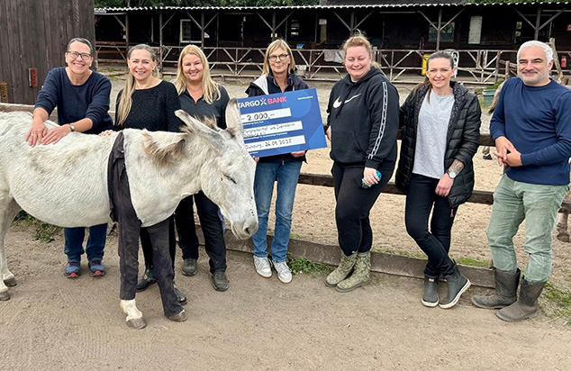 Eine Gruppe von Menschen steht neben einem Esel, während sie einen großen Scheck der TARGOBANK mit dem Betrag von 2.000 Euro präsentieren.