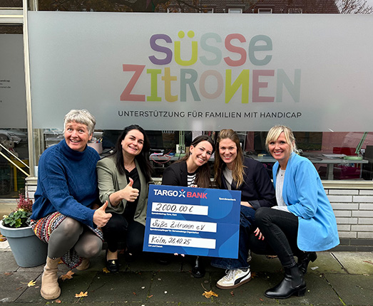 Fünf Personen posieren vor einem Fenster mit dem Schriftzug 'süsse Zitronen', während sie einen Scheck über 2000,00 € von der TARGOBANK halten.