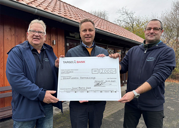 Drei Personen stehen vor einem Gebäude und halten einen großen Scheck der TARGOBANK über 2000 Euro für den Heimatverein Happerschmied. Der Scheck zeigt das Datum 30.11.2023 und den Vermerk 'Sankt Martin 2023'.