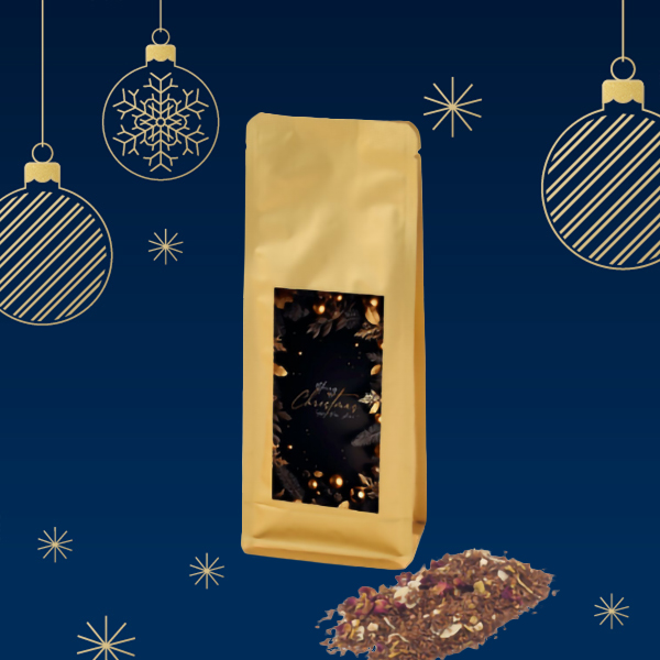 Eine goldene Tüte mit einer dunklen, festlichen Etikette und losem Teemischung auf einem blauen Hintergrund mit Weihnachtsornamenten.