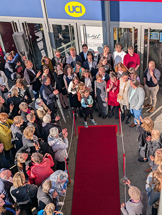 Eine Menschenmenge versammelt sich vor einem Kino mit einem roten Teppich und Absperrungen. Die UCI-Logos sind sichtbar.