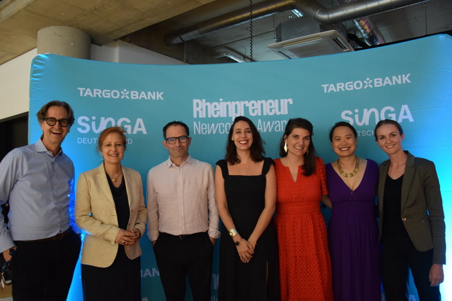 Eine Gruppe von Personen steht vor einem blauen Hintergrund mit dem Logo von TARGO BANK und der Aufschrift 'Rheinpreneur Newcomer Award' sowie 'SüGÄ Deutschland'.