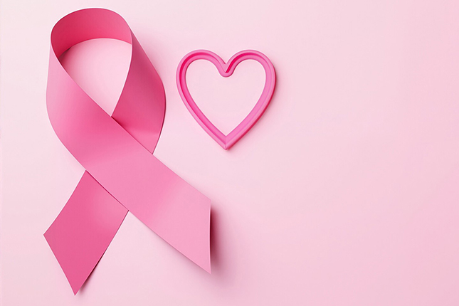 Ein pinkes Band und ein herzförmiger pinker Rahmen liegen auf einem hellrosa Hintergrund. Das Band symbolisiert das Bewusstsein für Brustkrebs.