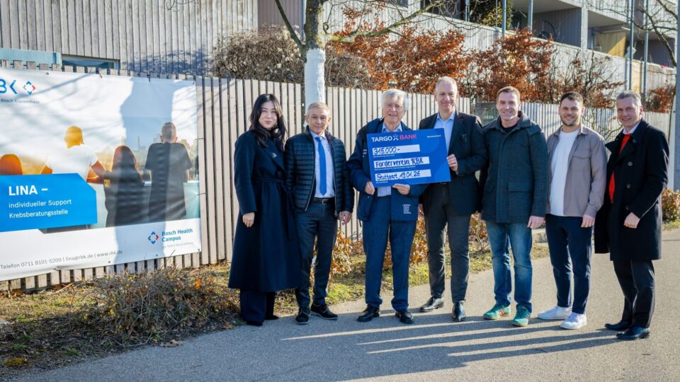 Eine Gruppe von Personen steht vor einem Banner, das Informationen über die Krebsberatungsstelle LINA enthält. Sie halten einen großen Scheck von 315.000 Euro für den Förderverein RBK. Der Hintergrund zeigt ein modernes Gebäude und Bäume, die im Winter keine Blätter haben.