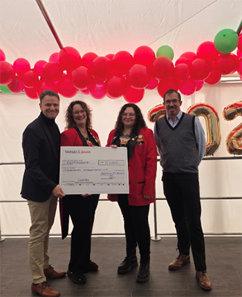 Vier Personen stehen unter einer Zeltplane mit roten und grünen Luftballons. Sie halten einen großen Scheck von TARGOBANK. Zwei Personen tragen formelle Kleidung, während die anderen beiden in rot gekleidet sind. Im Hintergrund sind goldene Zahlen "2023" zu sehen.