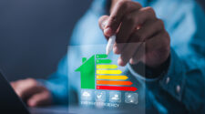 Eine Person hält einen Stift und zeigt auf ein digitales Diagramm zur Energieeffizienz, das eine Hausgrafik mit einer Farbskala von grün (A) bis rot (G) zeigt. Unterhalb sind Symbole für CO2, Pflanzen, Geld und Solarenergie zu sehen.