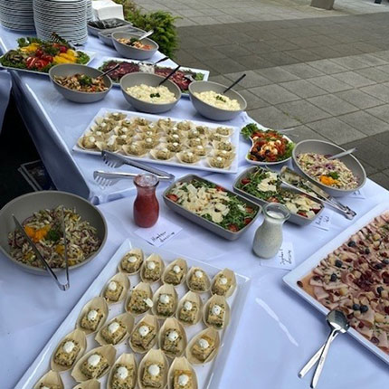 Ein reichhaltiges Buffet mit verschiedenen Gerichten auf einem Tisch. Es gibt mehrere Schalen mit Salaten, Gemüse und Pasta. Auf einem großen Teller sind kleine gefüllte Teigtaschen angeordnet. Daneben stehen Saucen und Dressings in Gläsern. Die Präsentation ist einladend, und das Ambiente wirkt freundlich und festlich.